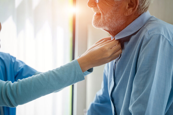 nurse helping older man get dressed in his room at care home