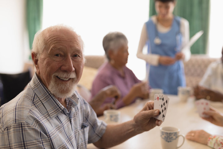 resident smiling playing cards in care home with other residents and staff around
